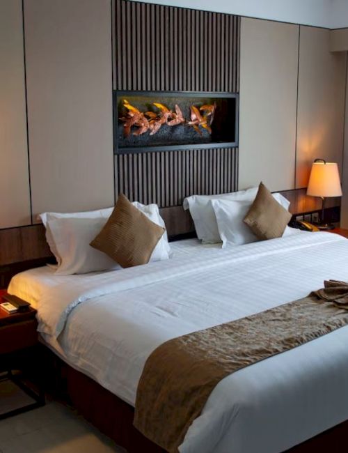 A neatly made bed in a modern hotel room with two bedside tables, lamps, decorative cushions, and a wall feature above the headboard.