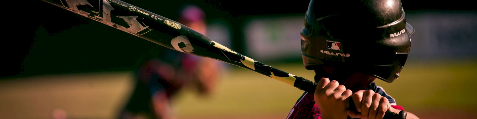 A person prepares to hit a pitched baseball, with a blurred background suggesting motion and focus on the batter.