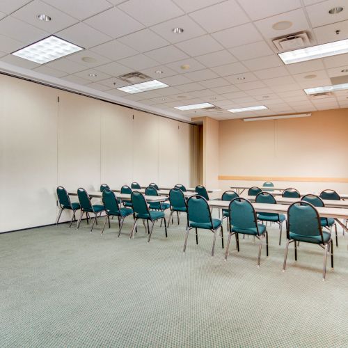 The image shows an empty conference room with long tables and chairs arranged in a U-shape under a fluorescent-lit ceiling.