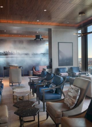 The image shows an upscale lounge area with modern seating, large windows offering a scenic waterfront view, and contemporary decor.